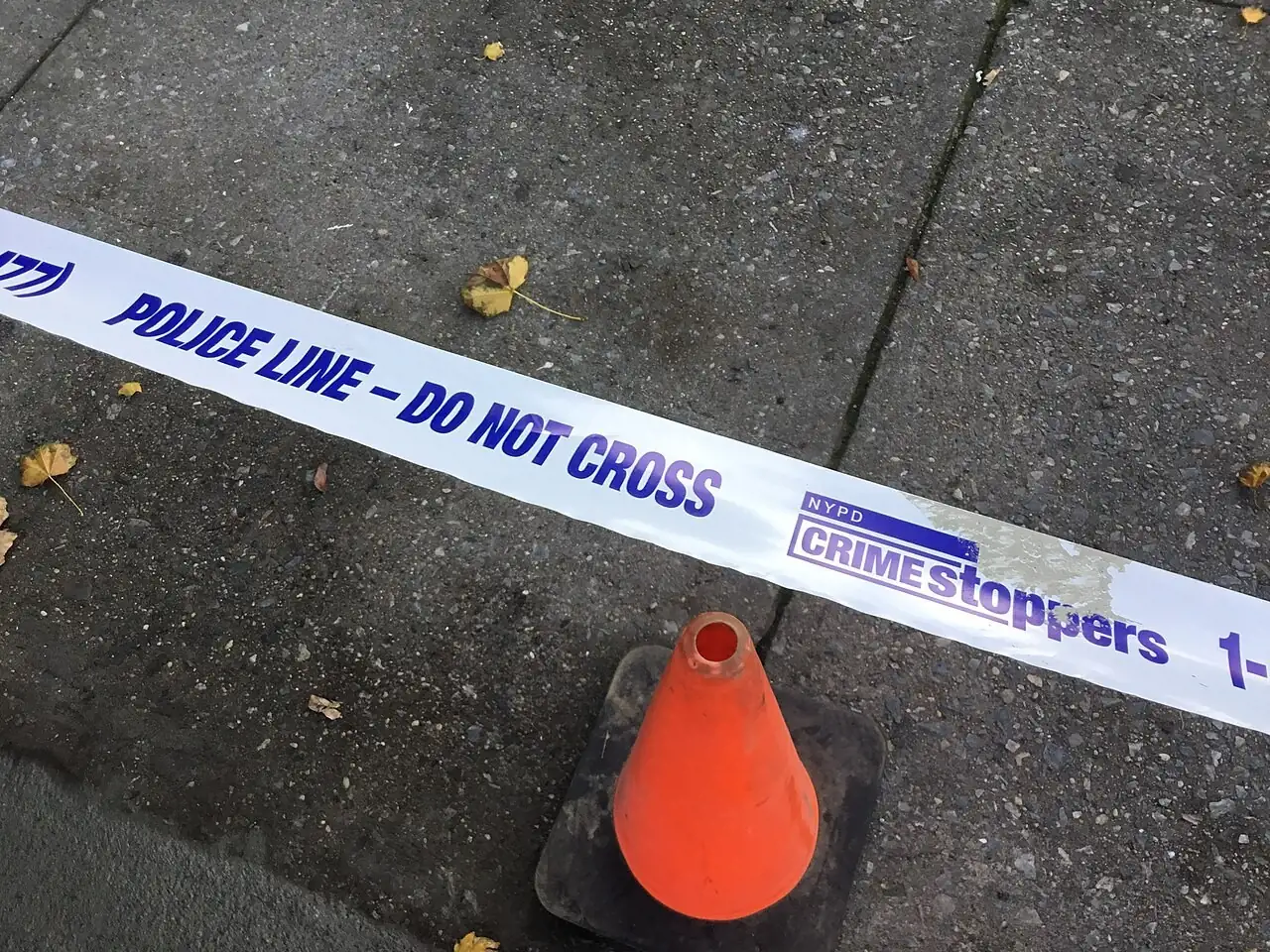 Police line tape above a traffic cone on a sidewalk